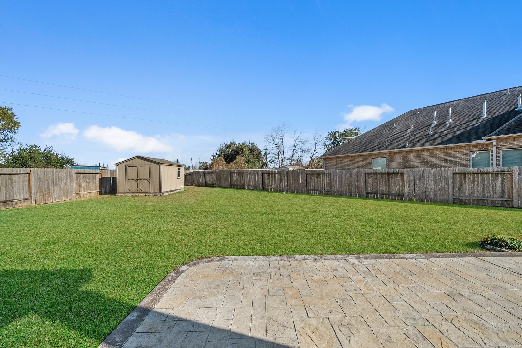 4747 Abercorn Street Rosharon, TX 77583 - Photo 35 of 46 This photo shows a spacious, fenced backyard with a well-maintained lawn, a storage shed, and a paved patio area, ideal for outdoor activities and gatherings.