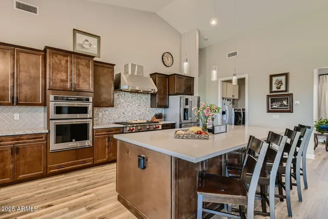 a large kitchen with stainless steel appliances a large counter top a stove a chimney a sink and a living room view