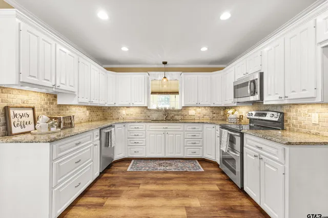 a kitchen with granite countertop white cabinets stainless steel appliances a sink and a counter top space