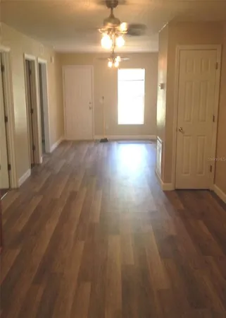 an empty room with wooden floor chandelier fan and windows