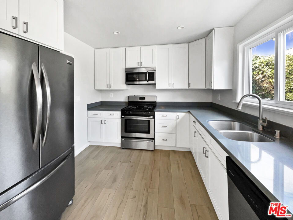 6906 Balcom Avenue Reseda, CA 91335 - Photo 6 of 19 a kitchen with granite countertop a refrigerator a sink a stove and microwave with wooden floor