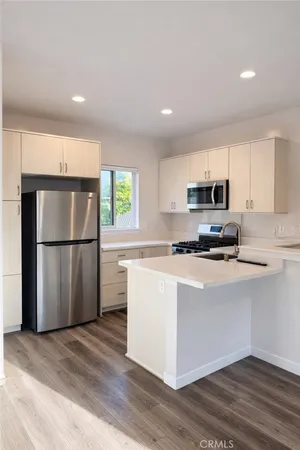 a kitchen with granite countertop a refrigerator a sink dishwasher a stove and white cabinets with wooden floor