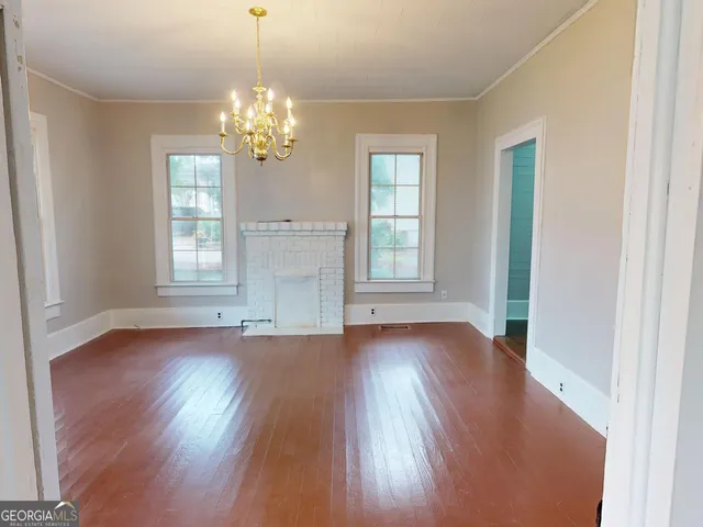 an empty room with wooden floor chandelier and windows