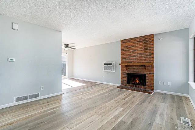 an empty room with wooden floor fireplace and windows
