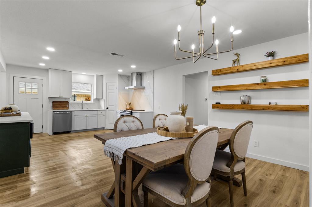 1917 South Vernon Avenue Dallas, TX 75224 - Photo 13 of 28 Open-concept living space featuring wood-finish flooring, a modern kitchen with white cabinetry and stainless steel appliances, a dining area with a brass chandelier, recessed lighting, and three substantial wood floating shelves