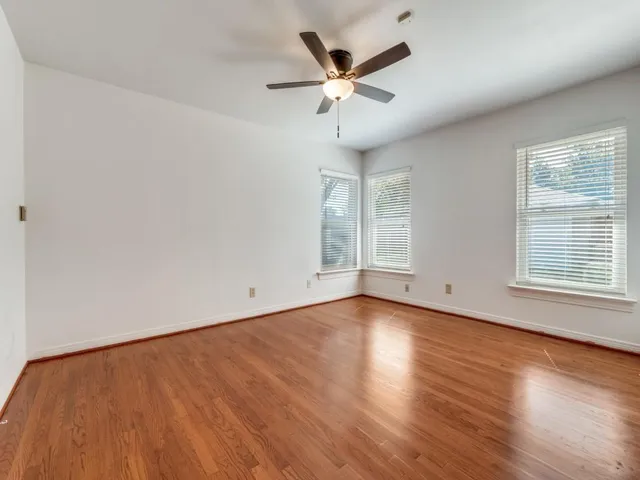 an empty room with wooden floor fan and windows