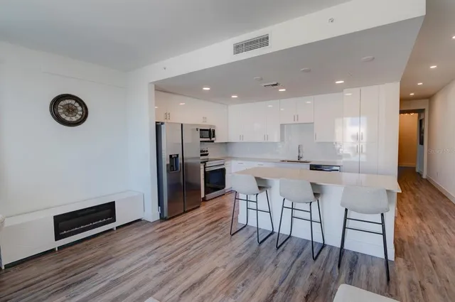 a kitchen with stainless steel appliances a refrigerator a stove top oven and a dining table with wooden floor