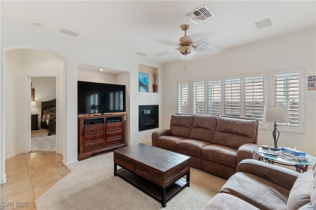 2078 Willow Bay Road Laughlin, NV 89029 - Photo 18 of 99 Family Room featuring a ceiling fan, arched walkways, a glass covered fireplace, light carpet, and light tile patterned floors