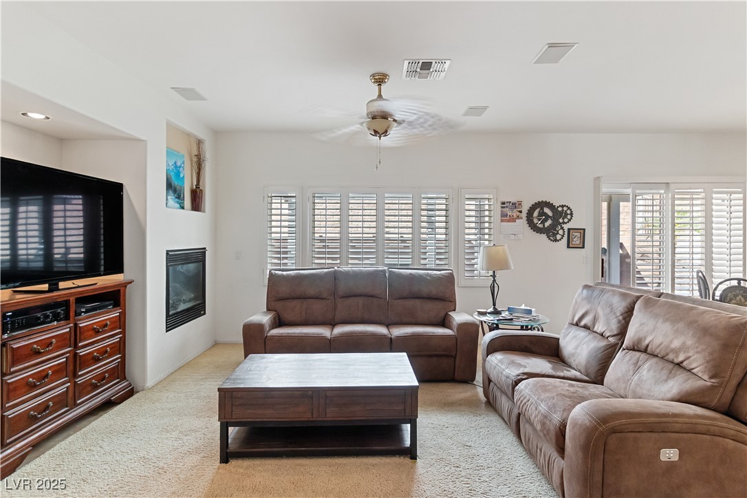2078 Willow Bay Road Laughlin, NV 89029 - Photo 20 of 99 Family Room featuring light carpet, a ceiling fan, and a glass covered fireplace