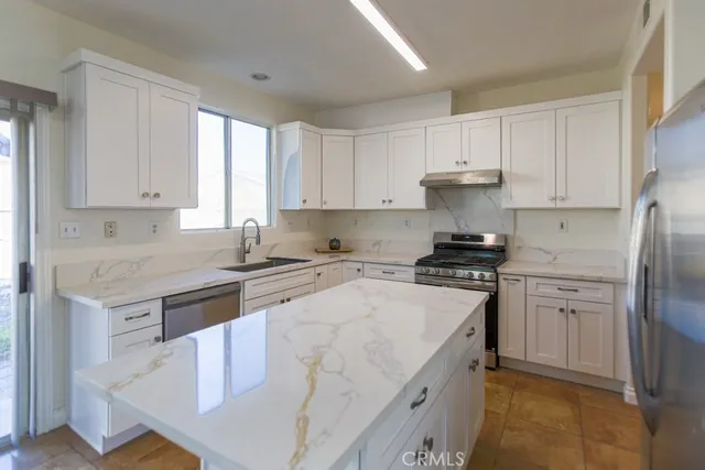 a kitchen with stainless steel appliances granite countertop a stove a sink a refrigerator and white cabinets