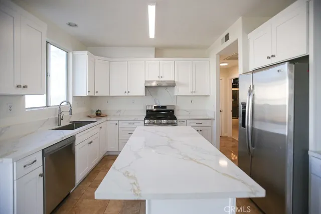 a kitchen with granite countertop a refrigerator stove and white cabinets