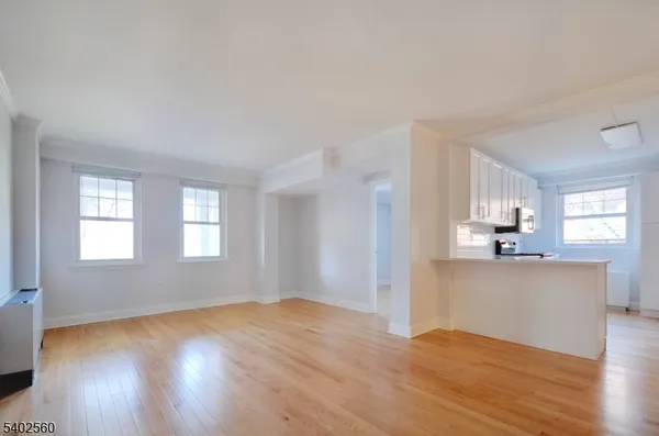 a view of a kitchen and an empty room with wooden floor and a window