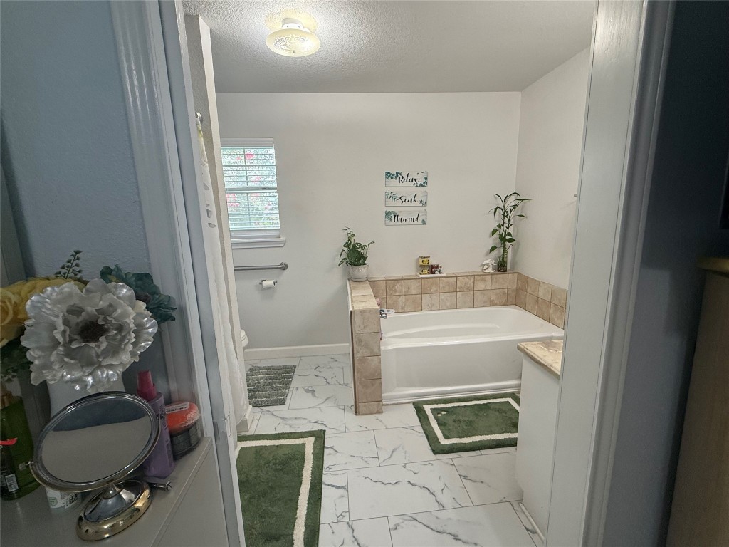 968 Red Town Road Elgin, TX 78621 - Photo 16 of 36 Bathroom with marble look tiles, a bath, and a textured ceiling