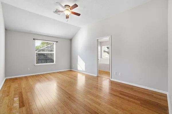 an empty room with wooden floor chandelier fan and windows