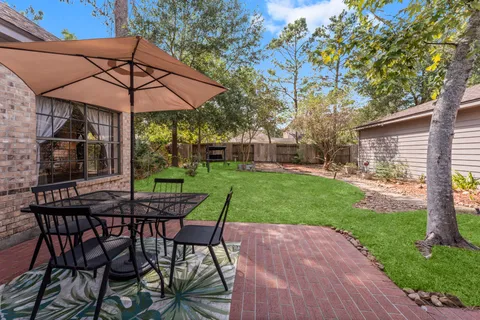 a view of a backyard with table and chairs under an umbrella with a barbeque grill and plants