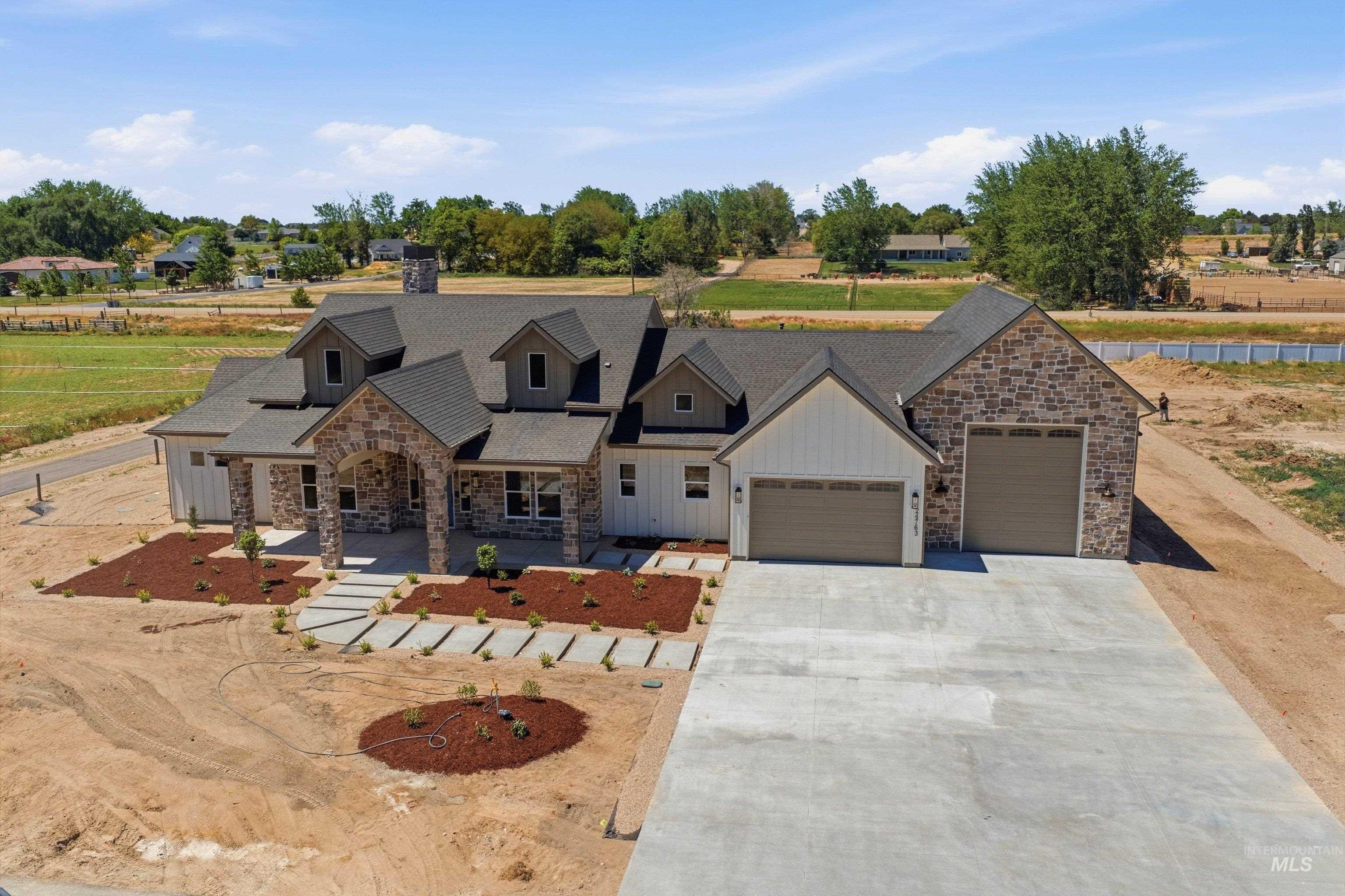 24763 Ardmore Court Caldwell, ID 83607 - Photo 42 of 50 Modern farmhouse architecture featuring stone and board-and-batten siding, a prominent covered entry, a multi-car garage with overhead doors, a gray shingled roof, and a concrete driveway