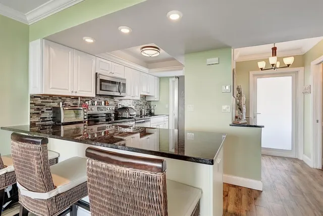 a kitchen with stainless steel appliances granite countertop a refrigerator a stove a sink a dining table and chairs with wooden floor