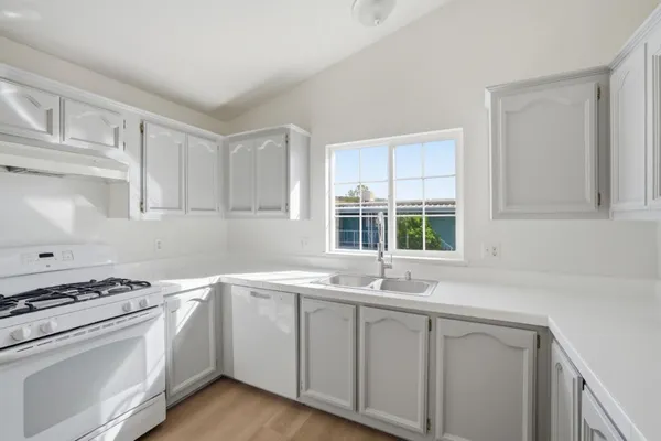 a view of a sink dishwasher a stove and cabinets