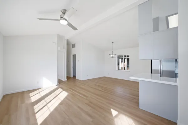 a view of empty room with wooden floor and kitchen view