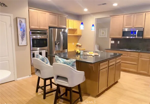 a kitchen with stainless steel appliances granite countertop a refrigerator a stove a sink a dining table and chairs with wooden floor