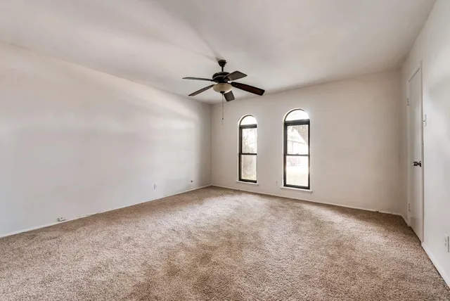 an empty room with chandelier fan and windows