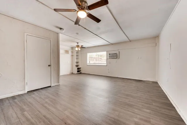 an empty room with wooden floor fan and windows