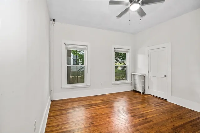 an empty room with wooden floor chandelier fan and windows