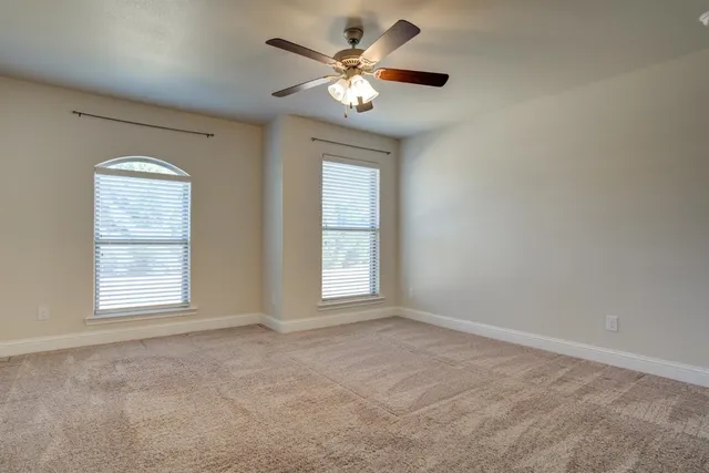 an empty room with chandelier fan and windows