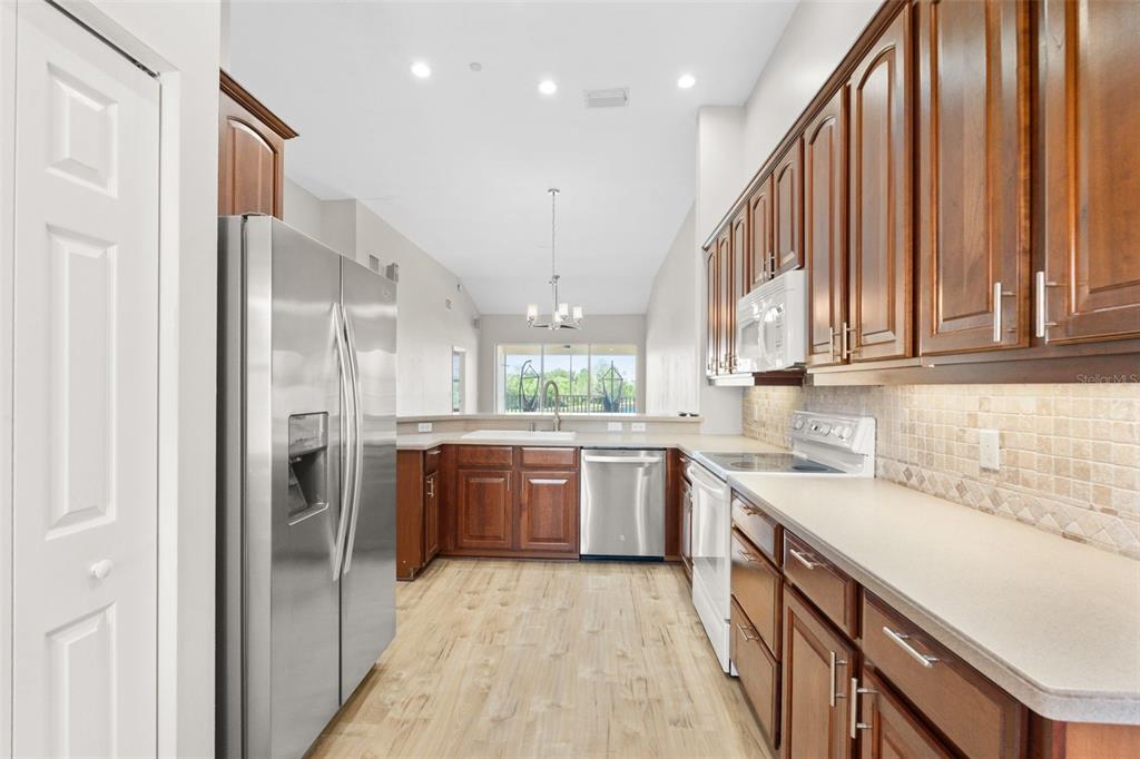 7187 Boca Grove Place, Unit 201 Lakewood Ranch, FL 34202 - Photo 8 of 48 a kitchen with stainless steel appliances granite countertop a refrigerator a sink dishwasher and a stove with wooden cabinets