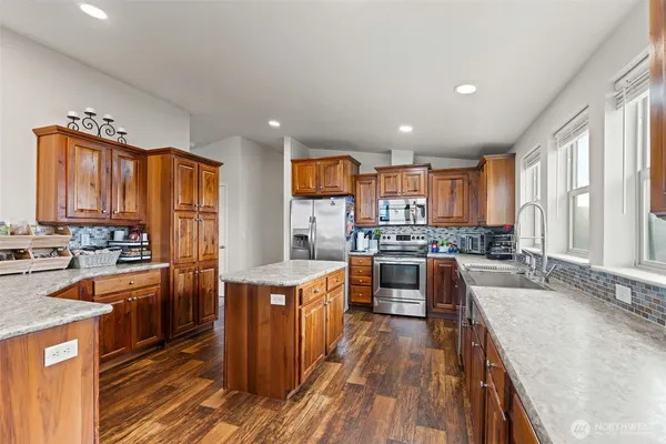 a kitchen with stainless steel appliances granite countertop wooden cabinets a sink dishwasher a stove and a refrigerator with wooden floor