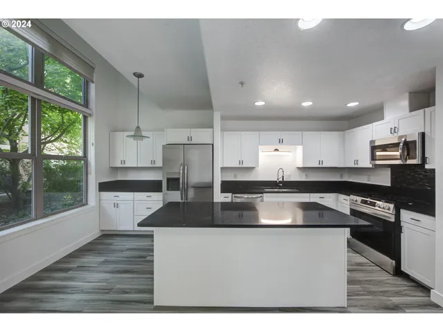 a kitchen with stainless steel appliances granite countertop a sink a stove a refrigerator a microwave oven with white cabinets and wooden floor