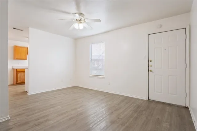 an empty room with wooden floor chandelier fan and windows