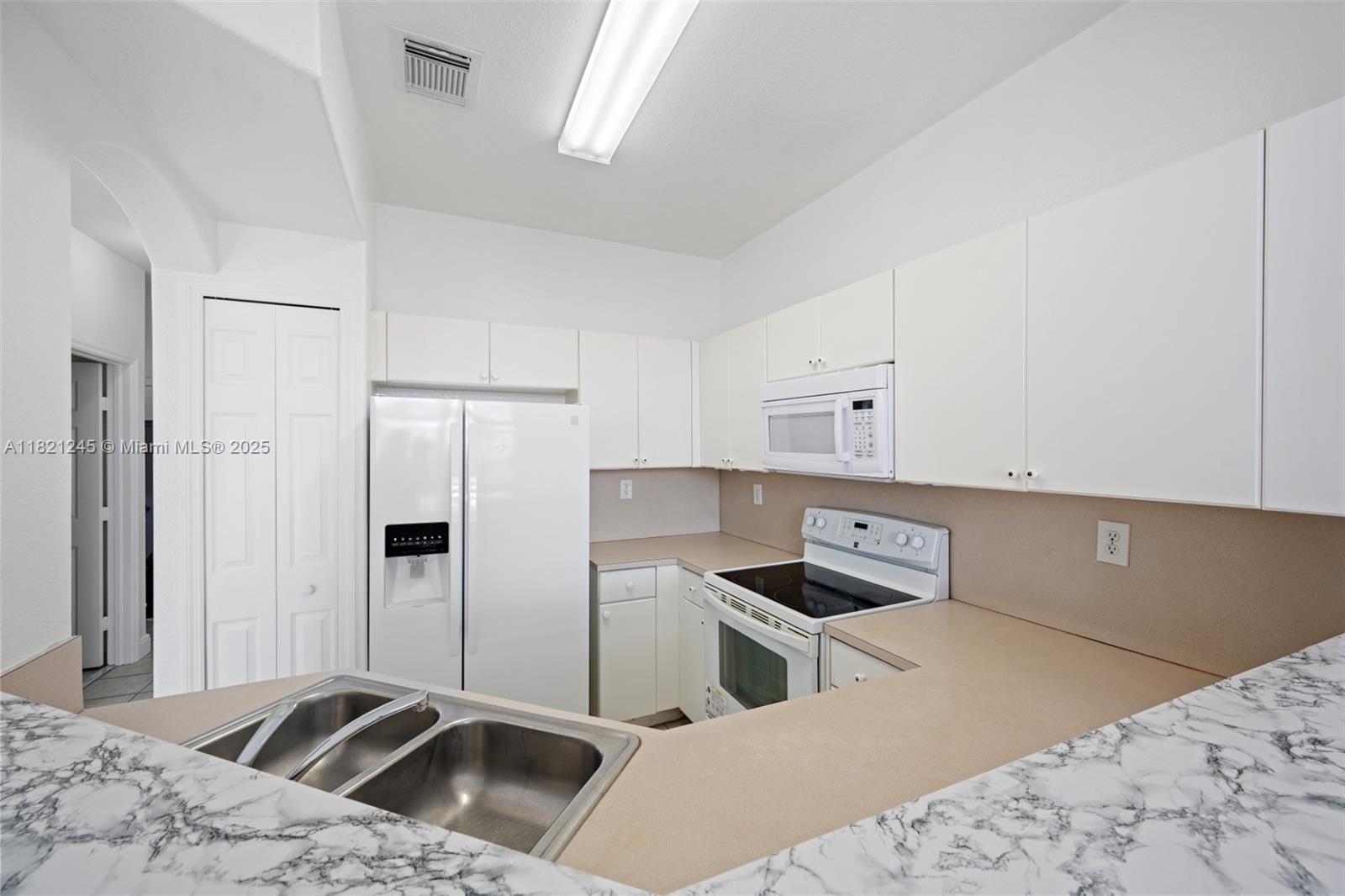 7633 Northwest 114th Path, Unit 7633 Doral, FL 33178 - Photo 21 of 25 a kitchen with stainless steel appliances kitchen island a refrigerator sink and white cabinets