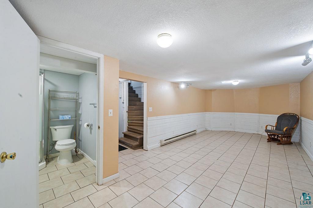 122 3rd Street Cloquet, MN 55720 - Photo 21 of 42 Spacious finished room featuring light-toned tile flooring, wainscoting, a full bathroom with shower, and access to a wooden staircase