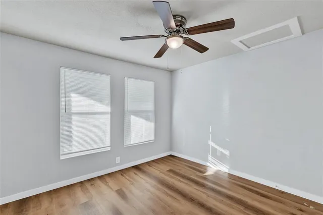 an empty room with wooden floor fan and windows