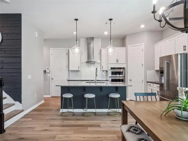 a open kitchen with stainless steel appliances granite countertop a stove a refrigerator a oven and a table with wooden floor