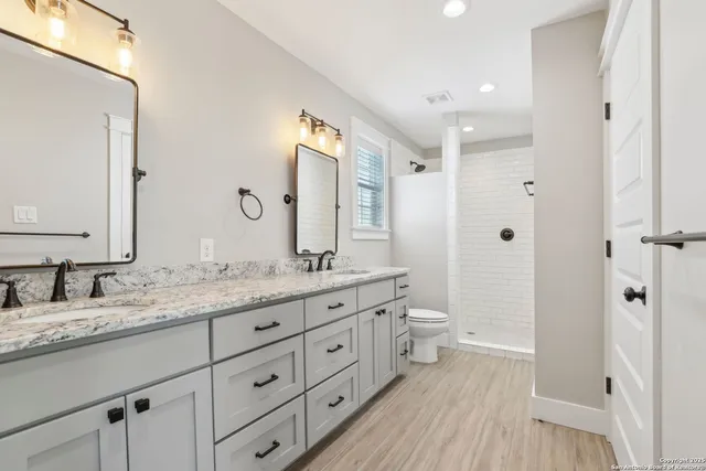 a bathroom with a granite countertop double vanity sink a mirror and a shower