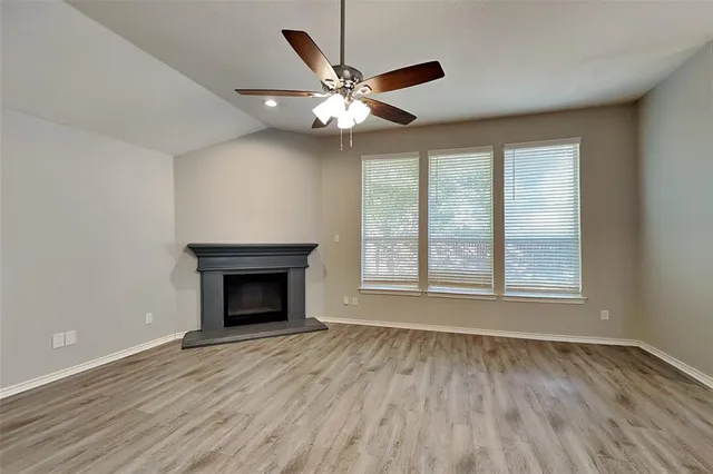 an empty room with wooden floor fan and windows
