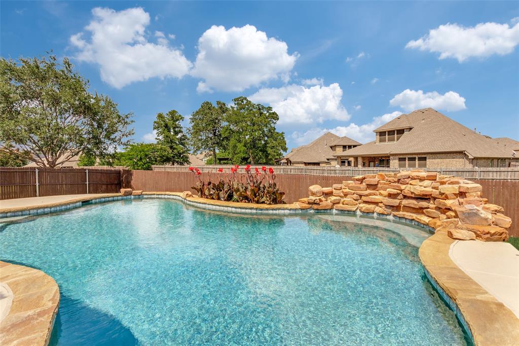 4117 Autumn Path Road Denton, TX 76208 - Photo 12 of 14 Freeform swimming pool featuring a rock waterfall, flagstone coping, and a surrounding privacy fence