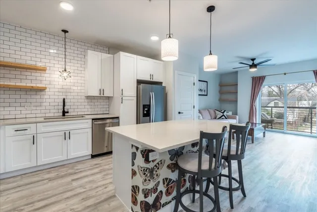 a kitchen with stainless steel appliances kitchen island granite countertop a stove a refrigerator a sink a dining table and chairs with wooden floor