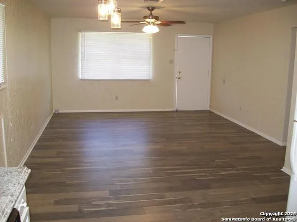 an empty room with wooden floor chandelier fan and windows