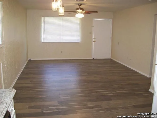 an empty room with wooden floor chandelier fan and windows