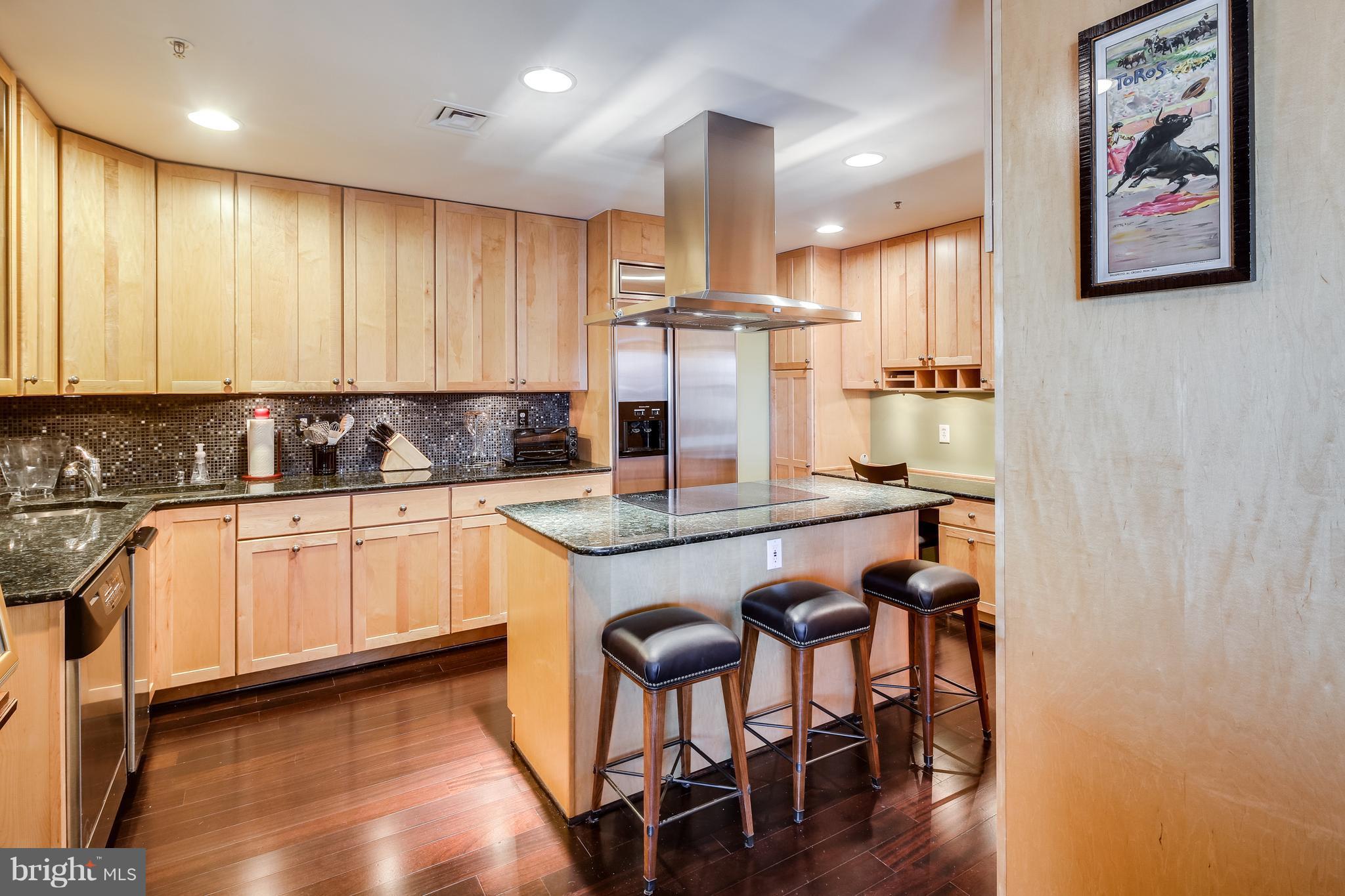 10 East Lee Street, Unit 1802 Baltimore, MD 21202 - Photo 7 of 21 a kitchen with kitchen island granite countertop wooden floors and refrigerator