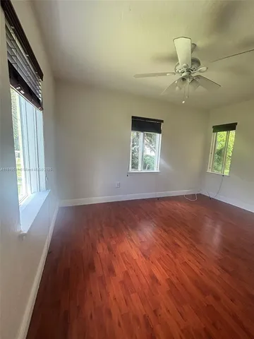 an empty room with wooden floor chandelier fan and windows
