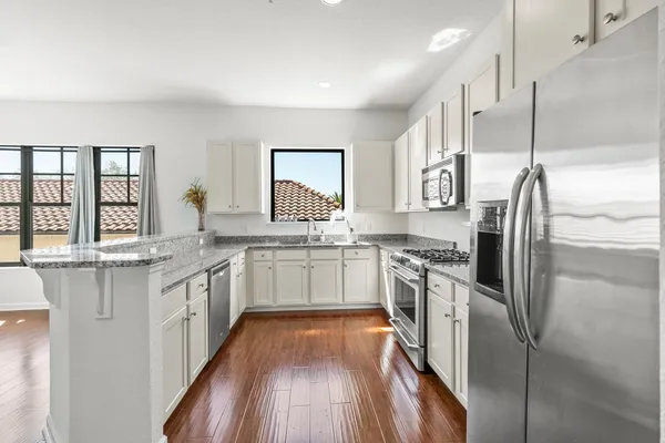 a kitchen with stainless steel appliances granite countertop a refrigerator a sink dishwasher a stove and white countertops with wooden floor