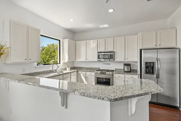 a kitchen with stainless steel appliances granite countertop a sink a stove a refrigerator with white cabinets and wooden floor