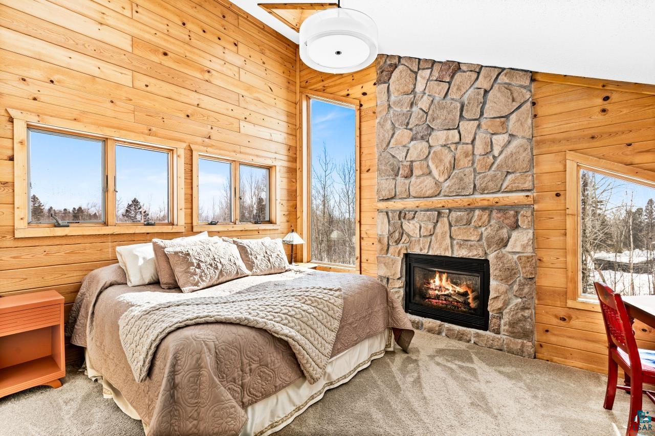 67 Snowshoe Trail Tofte, MN 55615 - Photo 5 of 42 Bedroom featuring carpet, wooden walls, multiple windows, and a fireplace