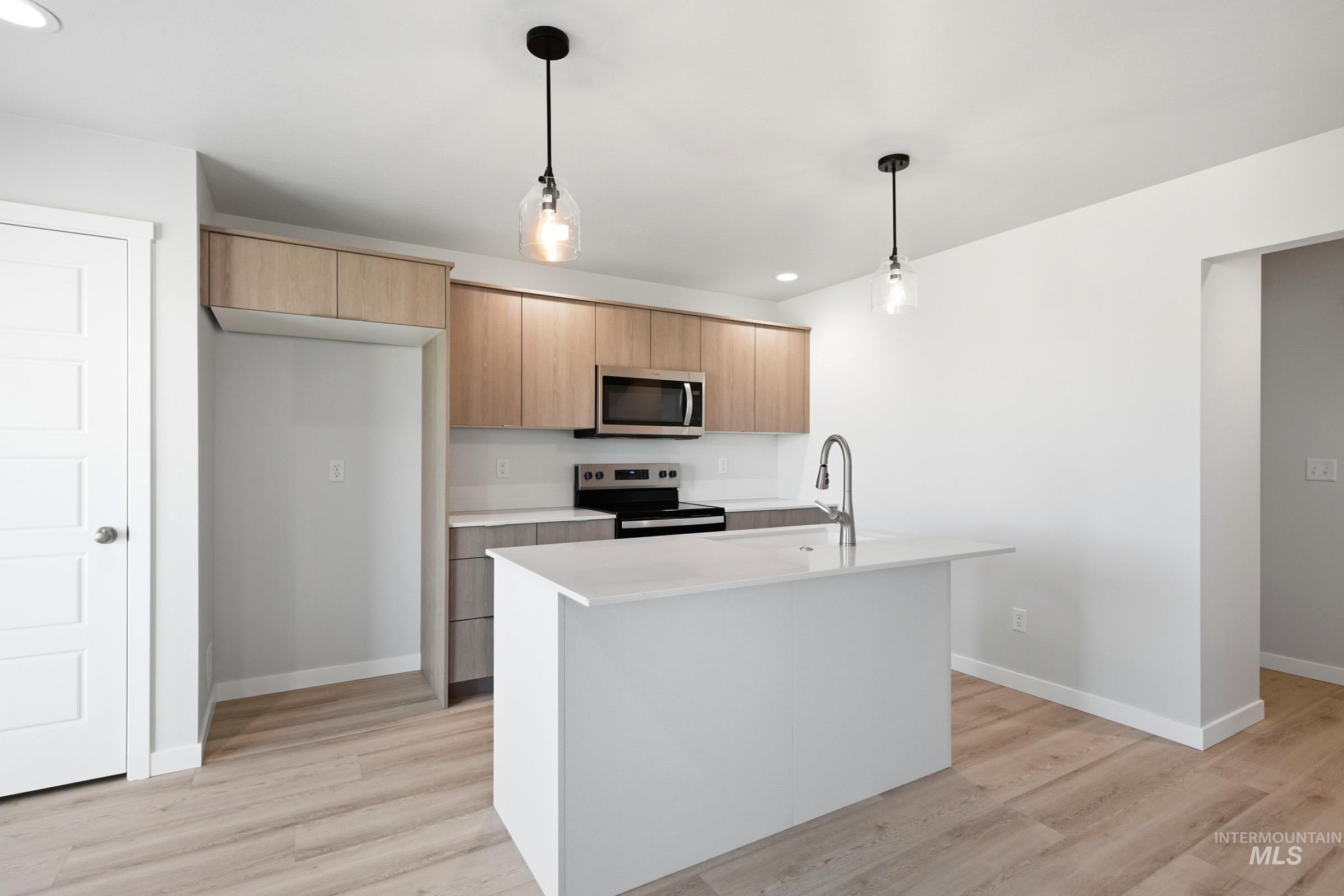 10812 Rutland Street Caldwell, ID 83605 - Photo 4 of 21 Bright kitchen featuring a central island with an integrated sink, light wood-finish cabinetry, stainless steel appliances including an oven and microwave, and wood-finish flooring