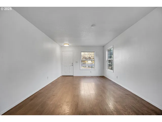 a view of an empty room with a window and wooden floor