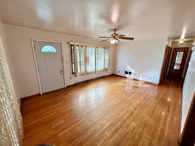 an empty room with wooden floor fan and windows